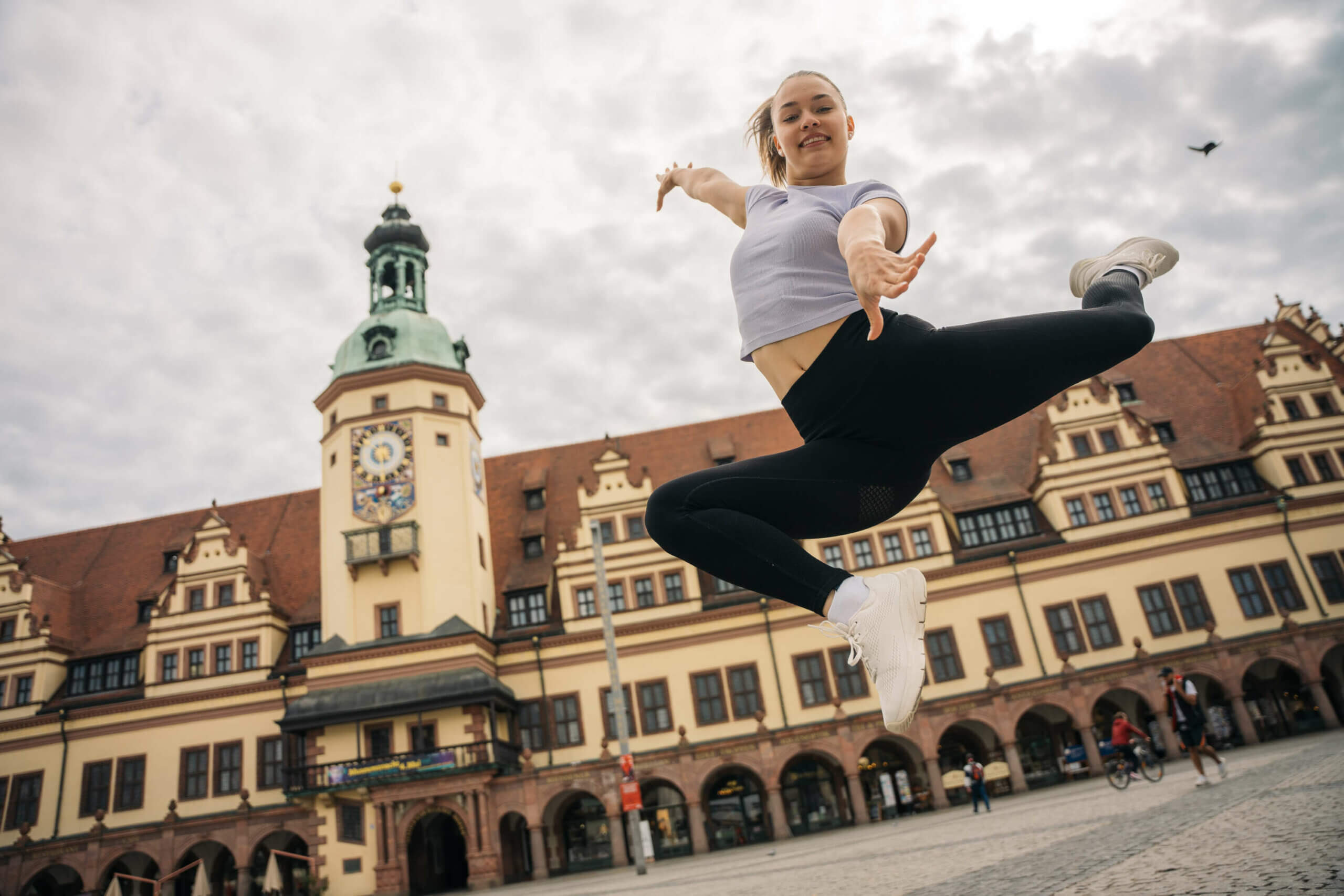 Eine Frau springt in die Höhe, die Beine angewinkelt zu einem gymnastischen Sprung vor dem Rathaus in Leipzig.
