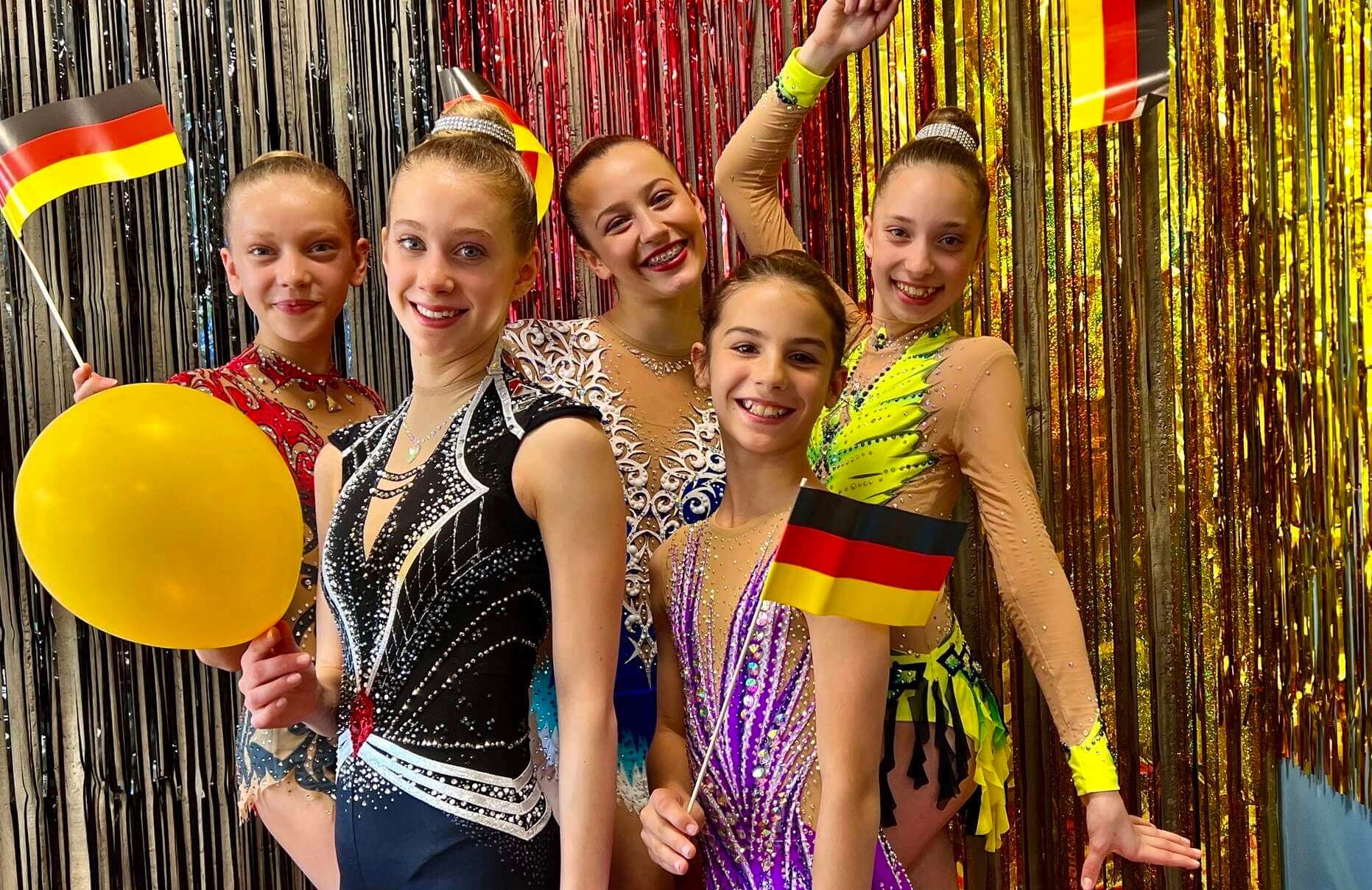 5 Gymnastinnen aus Hamburg beim Deutschlandcup 2024 bei einem Gruppenfoto, Drei halten ein Deutschlandfähnchen, ein einen gelben Luftballon in der Hand.