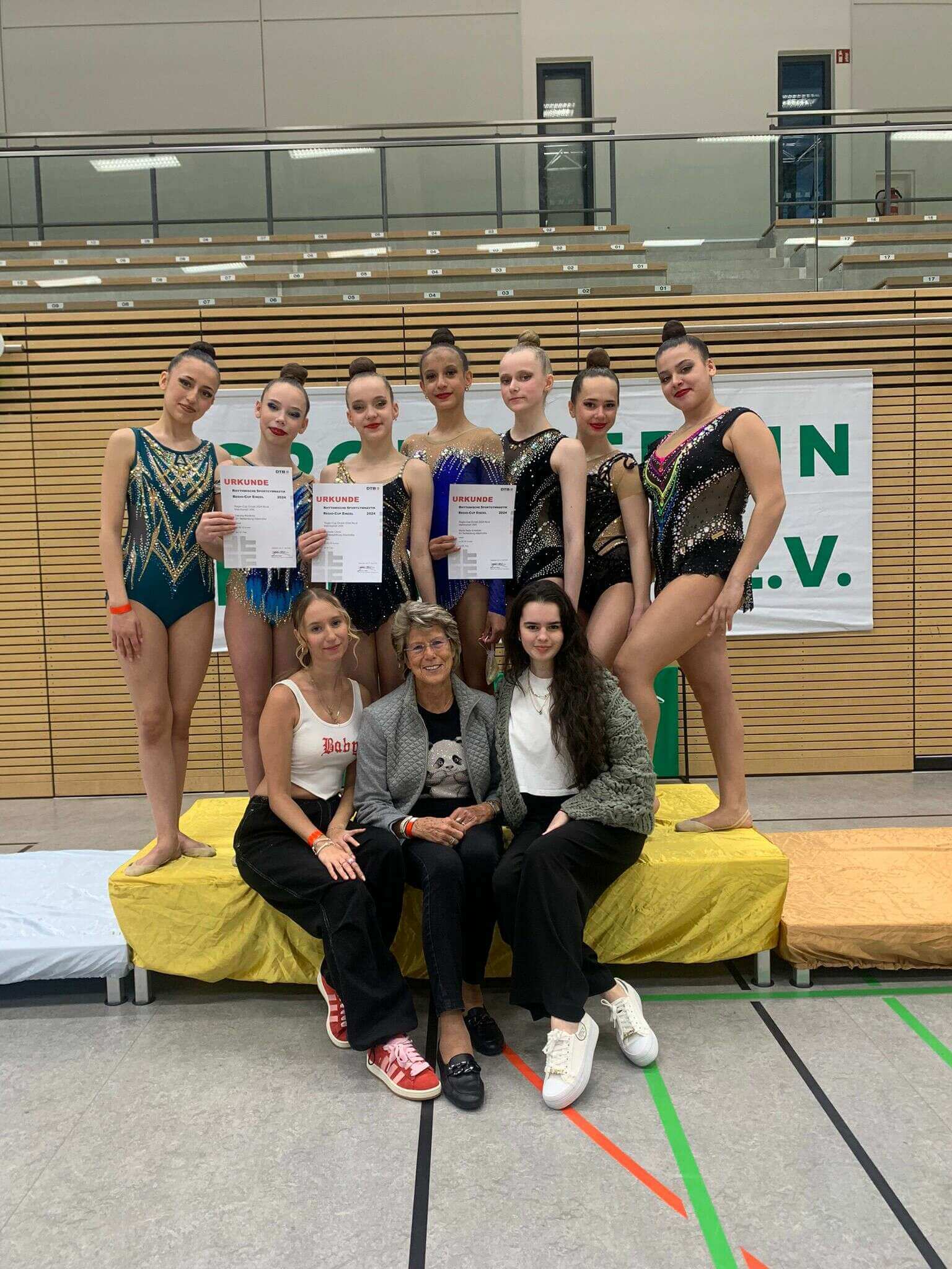 7 Gymnastinnen de SV Nettelburg-Allermöhe stehen auf einem Podest. Davor sitzen drei Frauen, zwei Trainerinnen und eine Funktionärin